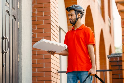 Courier delivers pizza to front door. Young deliveryman with safety helmet holding large yellow bag and cardboard box, outside, copy space photo