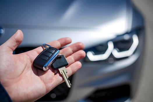Hand holding car keys in front of a blurred modern vehicle photo