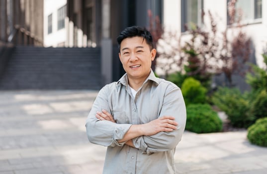 Portrait of confident asian entrepreneur posing with crossed arms and looking at camera near office building, outdoors. Ceo manager and boss, successful work photo