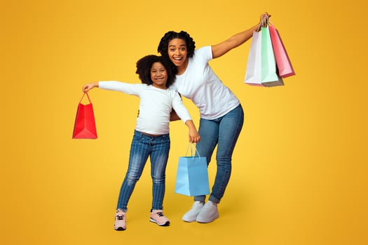Family Shopping. Portrait of joyful afro mother and daughter holding lot of bright shopper bags, posing over pink studio background, copy space photo