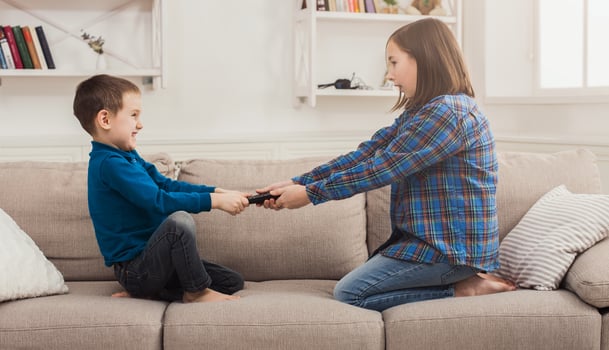 Siblings fighting over remote control at home, brother and sister have quarrel, copy space photo