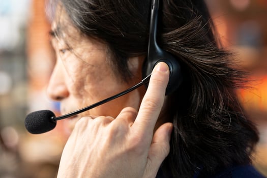 Call center staff member using headphones mic to answer technical inquiries about hardware issues. Knowledgeable Asian worker doing customer support job using PC to troubleshoot problems, close up photo