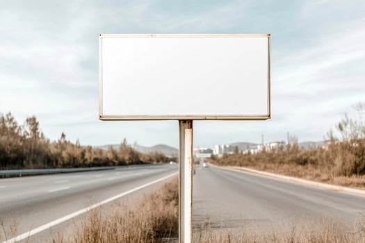 A large blank signboard stands beside a wide highway. The area is vibrant with open landscapes, moving vehicles, and a partly cloudy sky, ideal for advertising or directional purposes photo