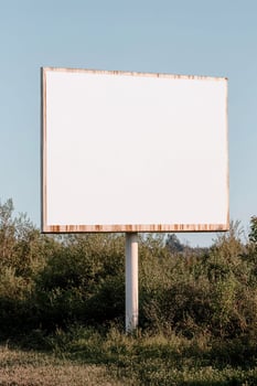 Set on a quiet country road, a large blank billboard stands alone amidst lush green fields under a clear blue sky, offering an inviting space for minimalistic branding opportunities photo