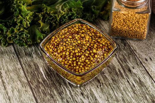 A bowl of mustard next to a glass jar photo