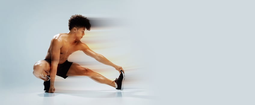 Fitness workout. Young shirtless athletic man exercising in extended leg squat pose, stretching legs and touching toes, demonstrating flexibility and strength over gray studio background photo
