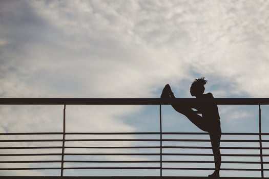 Stretching outdoors. Silhouette of african american woman athlete, doing exercise at stadium on blue sky with clouds background, free space photo