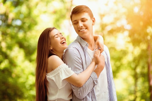Pretty young girl laughing and hugging her handsome boyfriend at summer park photo