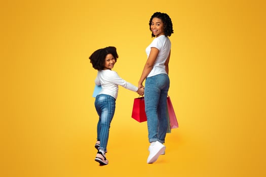 Successful Shopping. Happy Black Mother And Her Child Walking Together With Many Shopper Bags, Smiling Half Turned At Camera, Pink Background photo