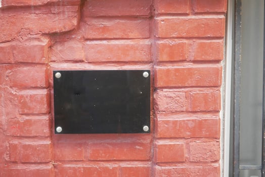 Black plaque mounted on red brick wall outside a building photo
