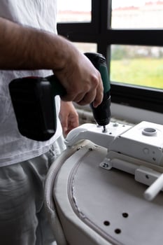 Young caucasian male using power drill to assemble furniture by window photo
