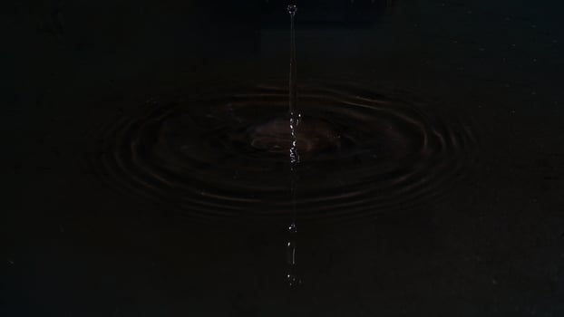 Water drops on the water surface forming waves isolated on black background photo