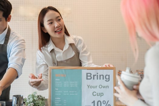 Sustainability and Customer Engagement. A barista explains the benefits of bringing a personal cup to a customer at a trendy cafe. photo