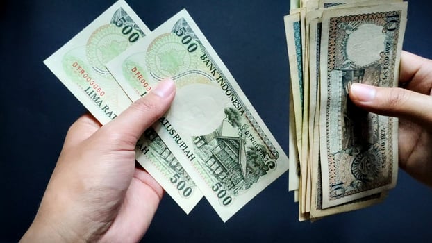 A person's hand is seen counting old rupiah banknotes of Rp10 to Rp500, isolated on a black background. Close-up view photo