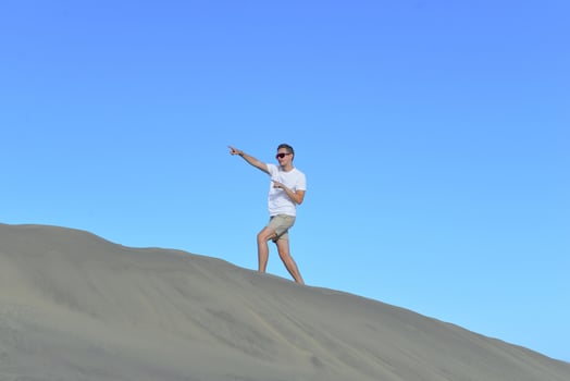 A young man walking along a dune through barkhan in Maspalomas, Gran Canaria on a hot sunny day. A self confident man goes up the mountain - success and achievements concept photo