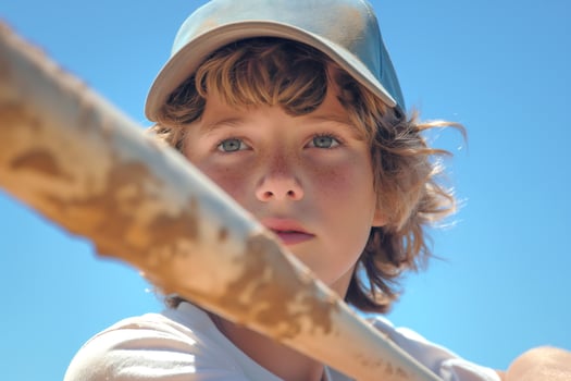 A young boy with curly hair and freckles gazes thoughtfully toward the horizon while holding a baseball bat. photo