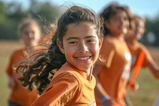 A joyful Hispanic girl, around 10 years old, smiles brightly while running with friends in an outdoor sports setting. photo