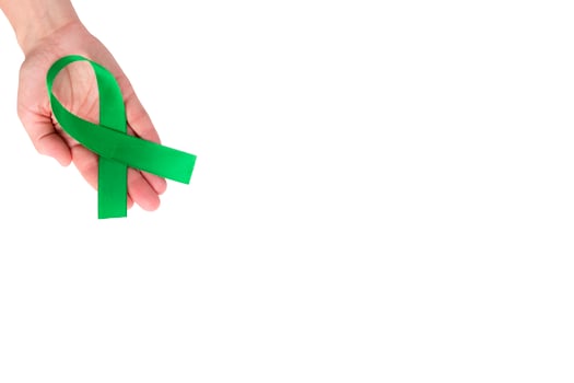 Green satin ribbon on the palm of a woman, isolated on a white background. Cancer awareness symbol. copy space photo