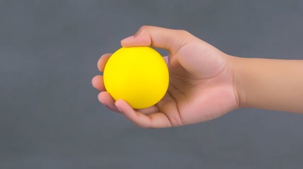Close up of a Hand Holding a Small Yellow Sphere Against a Gray Background photo