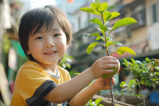 Happy Asian boy smiling while picking fruit from a small tree, surrounded by vibrant green foliage. photo