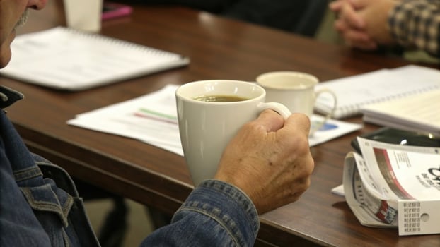 person holding coffee mug during meeting at table with documents and notebooks. setting suggests casual yet focused atmosphere, with participants engaged in discussion photo