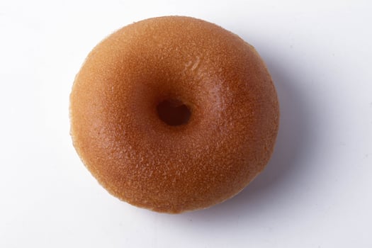 plain, glazed donut sits on white background, showcasing its smooth texture and classic round shape. donut golden brown color highlights its freshly baked appearance photo