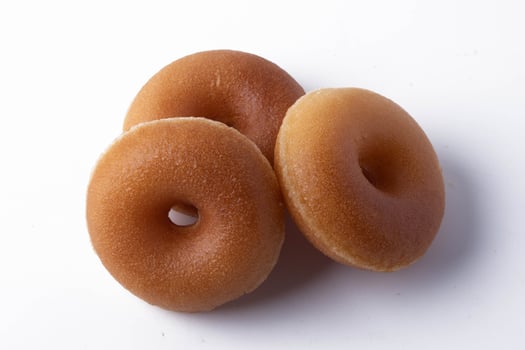 Three delicious glazed donuts are arranged on white background, showcasing their golden brown color and smooth texture. donuts appear fresh and inviting, perfect for sweet treat photo