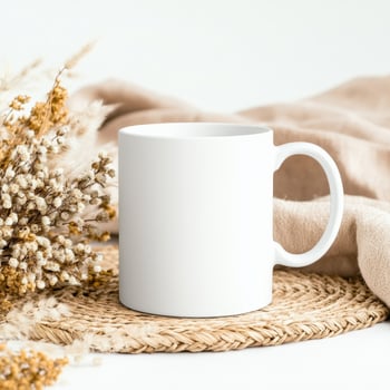 white mug placed on woven mat with dried flowers and soft fabric, creating serene and cozy atmosphere. Perfect for showcasing designs or branding photo