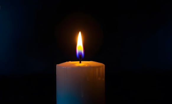 A single candle is lit in the dark photo