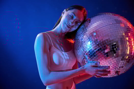 Holding mirrored ball in the club. Young woman in underwear is in the studio with neon lights photo