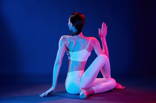 Rear view.. Sitting and doing exercises. Young woman in sportive clothes is in the studio with neon lights photo