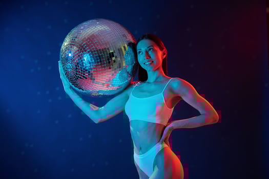 Party time. Holding mirrored ball. Young woman in underwear is in the studio with neon lights. photo