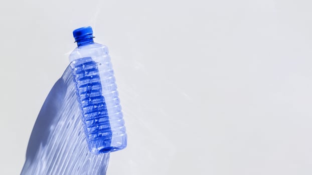 Transparent plastic bottles with blue caps and sun shadows on light background. Top view Water bottles at natural light. Themes of recycling, sustainability, water conservation, minimal style photo