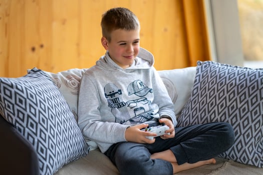 A boy in a gray sweatshirt plays on a game console while sitting on the sofa. photo
