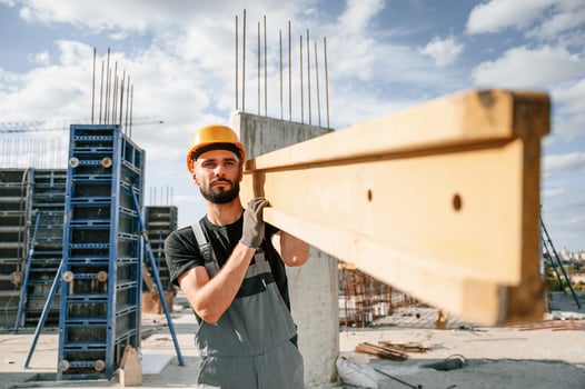 Carrying wooden plank. Man in uniform is working on the construction site. photo