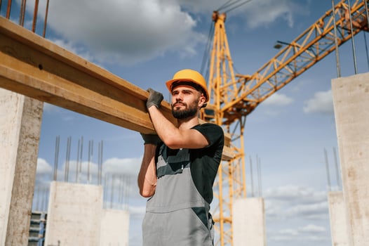 Front view of man that is in uniform holding wooden plank on the construction site photo