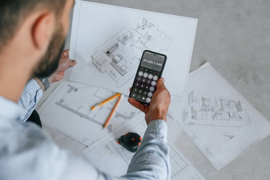 Calculating ,numbers, by using smartphone. Plan is on the floor. The man is making repairs in the apartment photo
