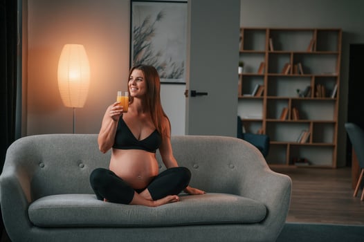 Sitting on the ,sofa, and drinking orange juice. Beautiful pregnant woman is indoors at home photo