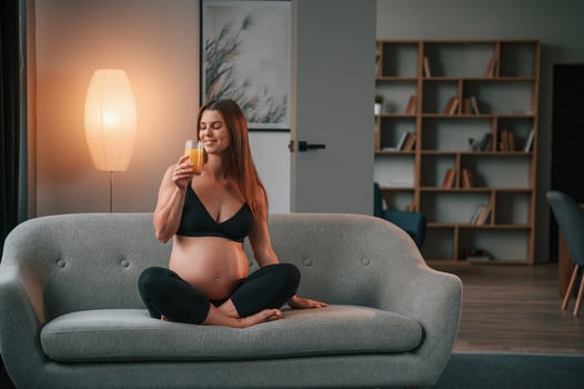 Sitting on the ,sofa and drinking orange juice. Beautiful pregnant woman is indoors at home photo