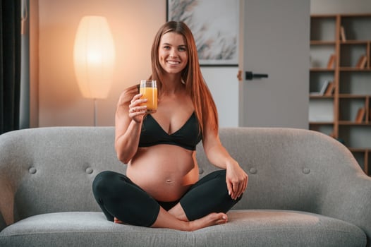 Sitting on the sofa and drinking ,orange juice. Beautiful pregnant woman is indoors at home photo