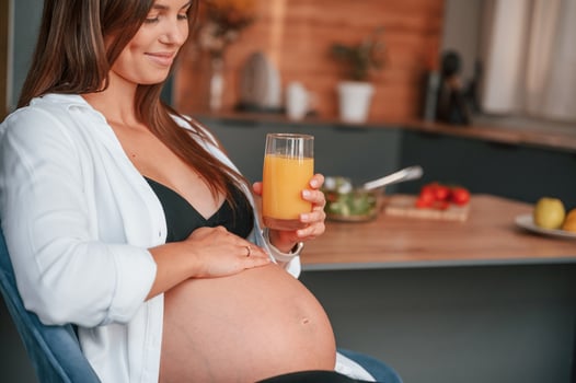 Touching belly and holding glass with orange juice. Beautiful pregnant woman is indoors at home photo