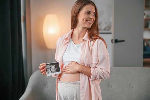 Holding ,ultrasound diagnostics picture of the baby. Beautiful pregnant woman is indoors at home photo
