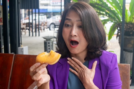 Woman sitting outside at cafe holding donuts in hand shocked face surprised eating tasty donuts delicious enjoy eating food free time lifestyle concepts photo
