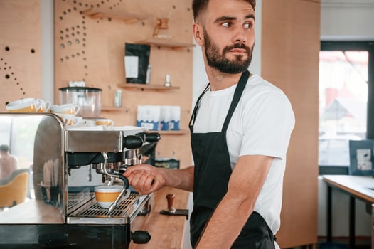 Using ,coffee machine.. Cafe worker in white shirt and black apron is indoors photo