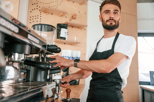 Preparing the coffee machine. Cafe worker in white shirt and black apron is indoors photo