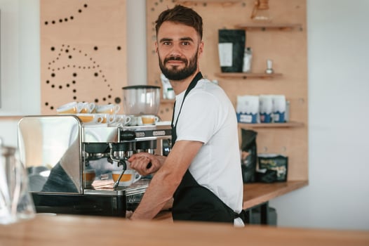 Busy by working with coffee ,machine. Cafe worker in white shirt and black apron is indoors photo