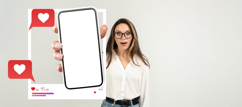 A young influencer with glasses is excitedly holding a smartphone with a blank screen. The background is isolated, highlighting her engaging expression and the potential for social media interaction. photo