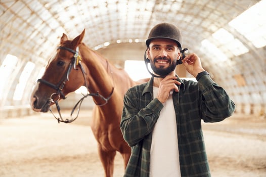 Wearing protective hat and smiling. Young man with a horse is in the hangar photo
