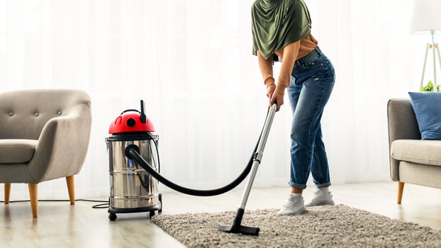 A young woman is actively vacuuming the living room of her home. She wears casual attire and is focused on cleaning the carpet, creating a fresh and tidy space. photo