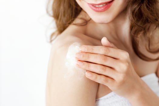 Cropped of young woman wrapped in towel applying lotion on shoulder, copy space photo